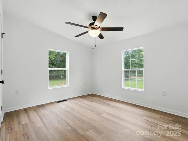 an empty room with wooden floor ceiling fan and windows