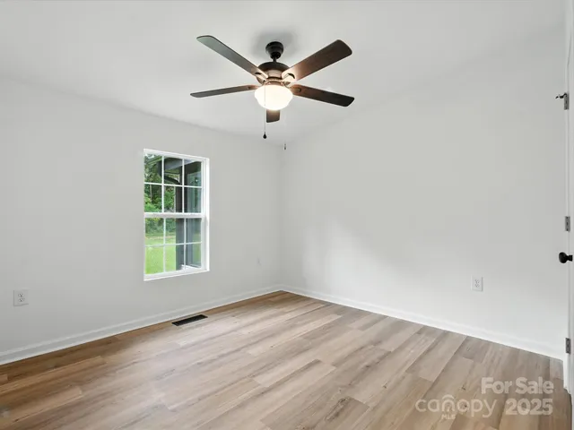 an empty room with wooden floor fan and windows