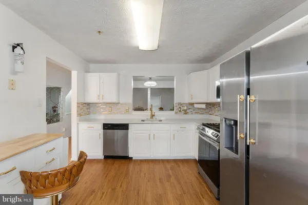 a kitchen with stainless steel appliances granite countertop a refrigerator a sink dishwasher a stove and white countertops with wooden floor