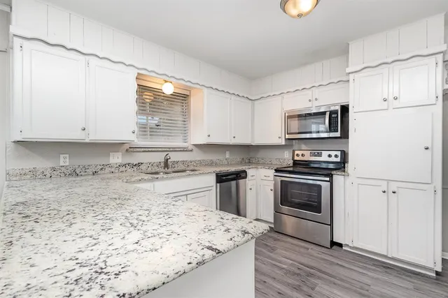 a kitchen with granite countertop a sink stainless steel appliances and white cabinets