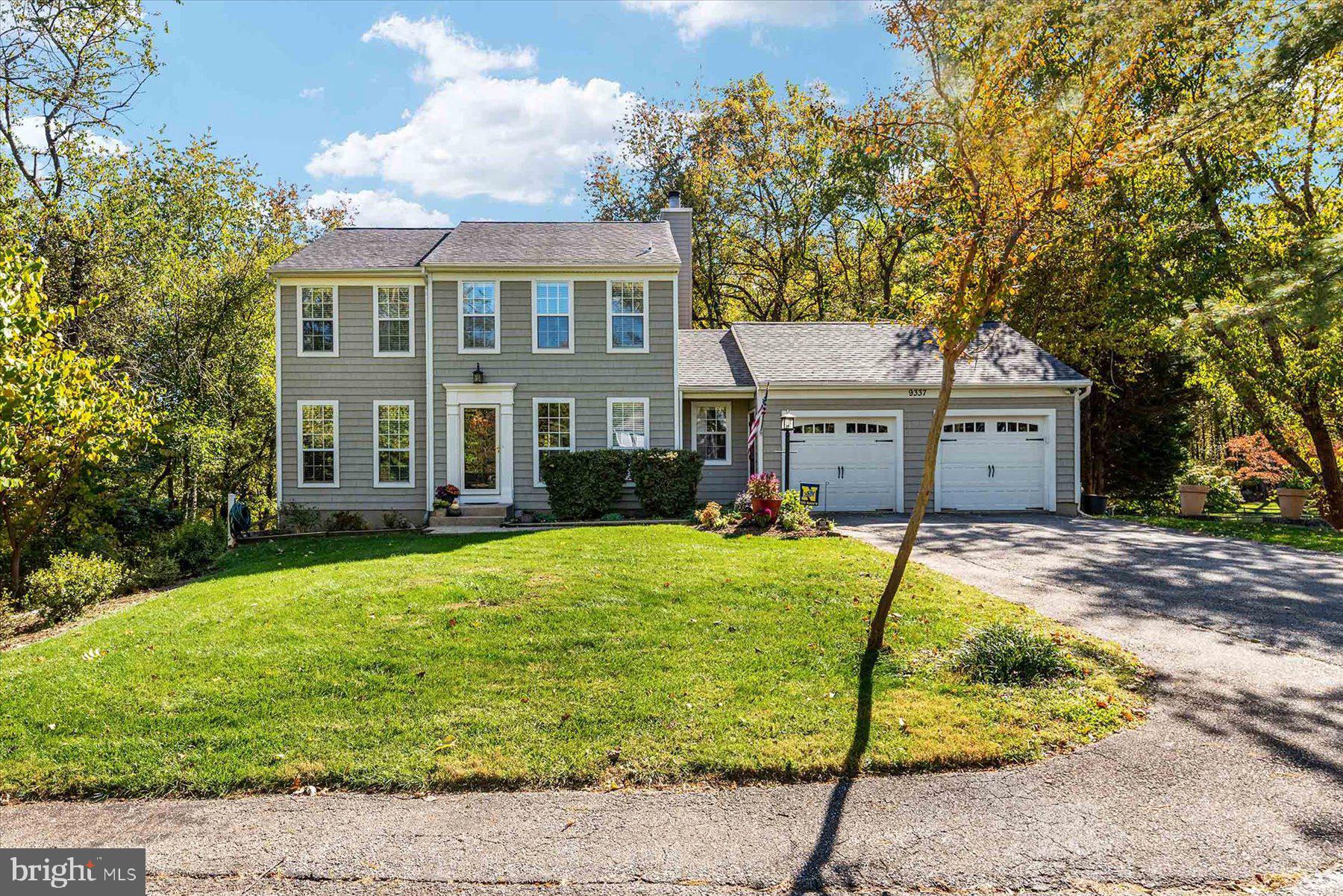 a view of a white house next to a yard with a fountain and large trees
