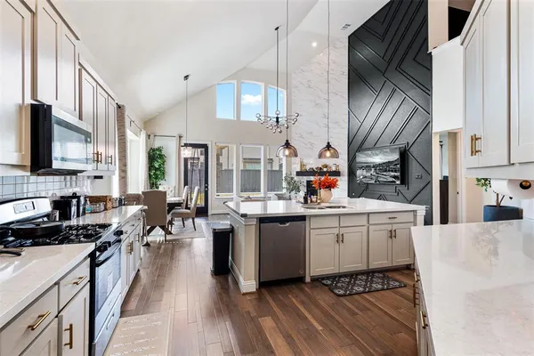 a kitchen with stainless steel appliances a sink dishwasher a stove top oven a dining table and chairs with wooden floor