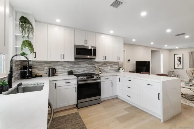 a large white kitchen with stainless steel appliances granite countertop a stove a sink a refrigerator a microwave and cabinets