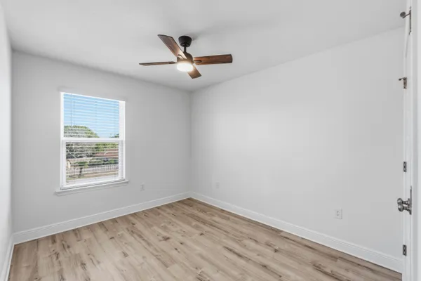 an empty room with wooden floor ceiling fan and windows