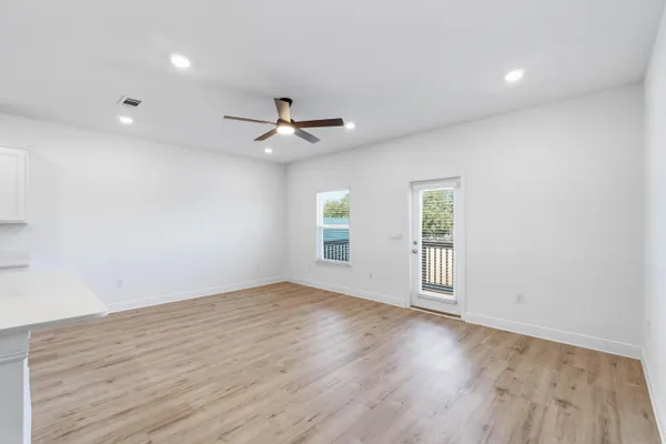 an empty room with wooden floor ceiling fan and windows