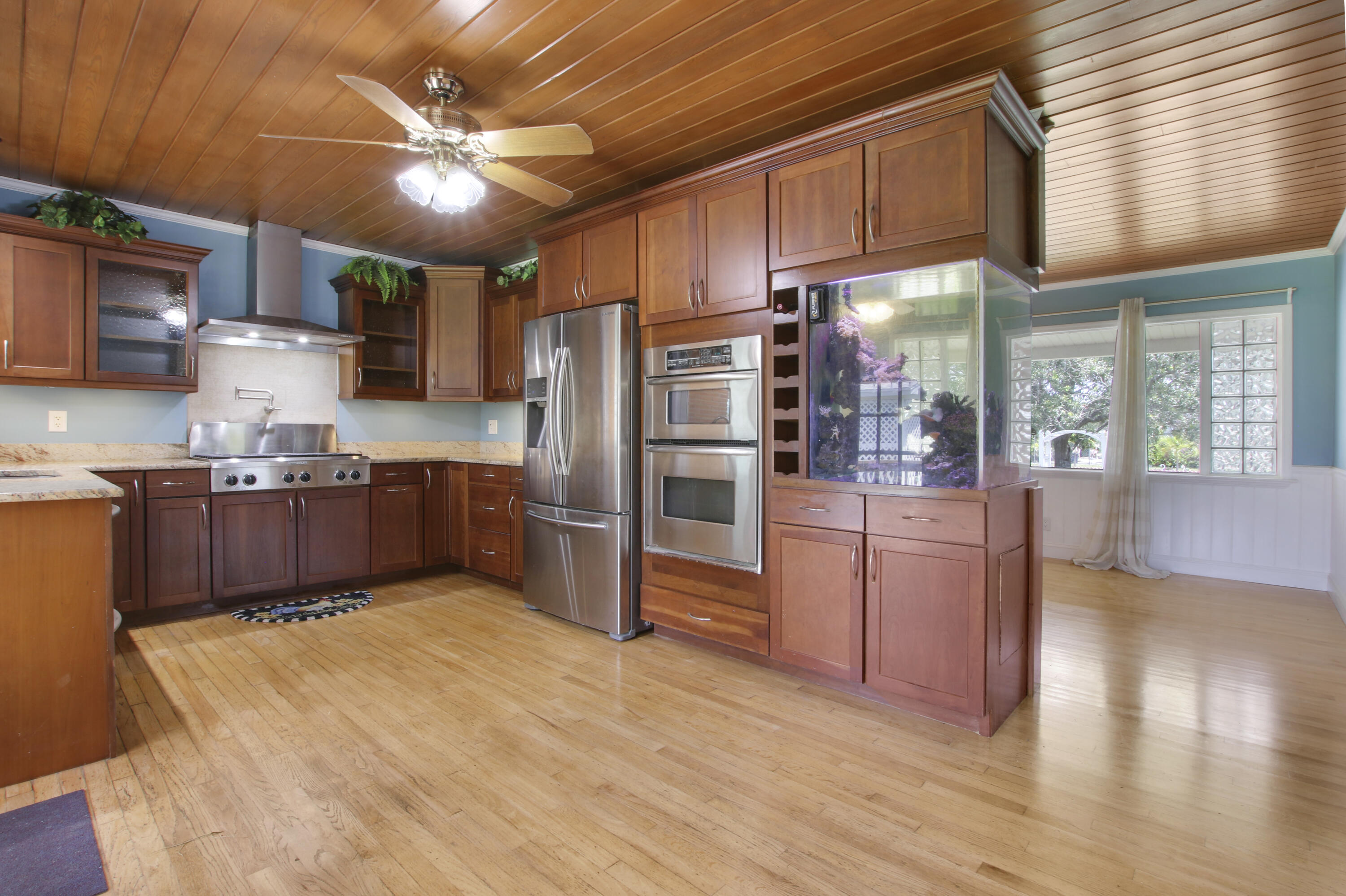a kitchen with stainless steel appliances kitchen island granite countertop a refrigerator oven stove a sink a dining table and chairs with wooden floor