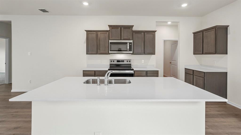 216 Pheasant Run Road Terrell, TX 75160 - Photo 29 of 37 Spacious kitchen island with a built-in sink, stainless steel faucet, white countertops, gray wood-finish cabinetry, and wood-finish flooring