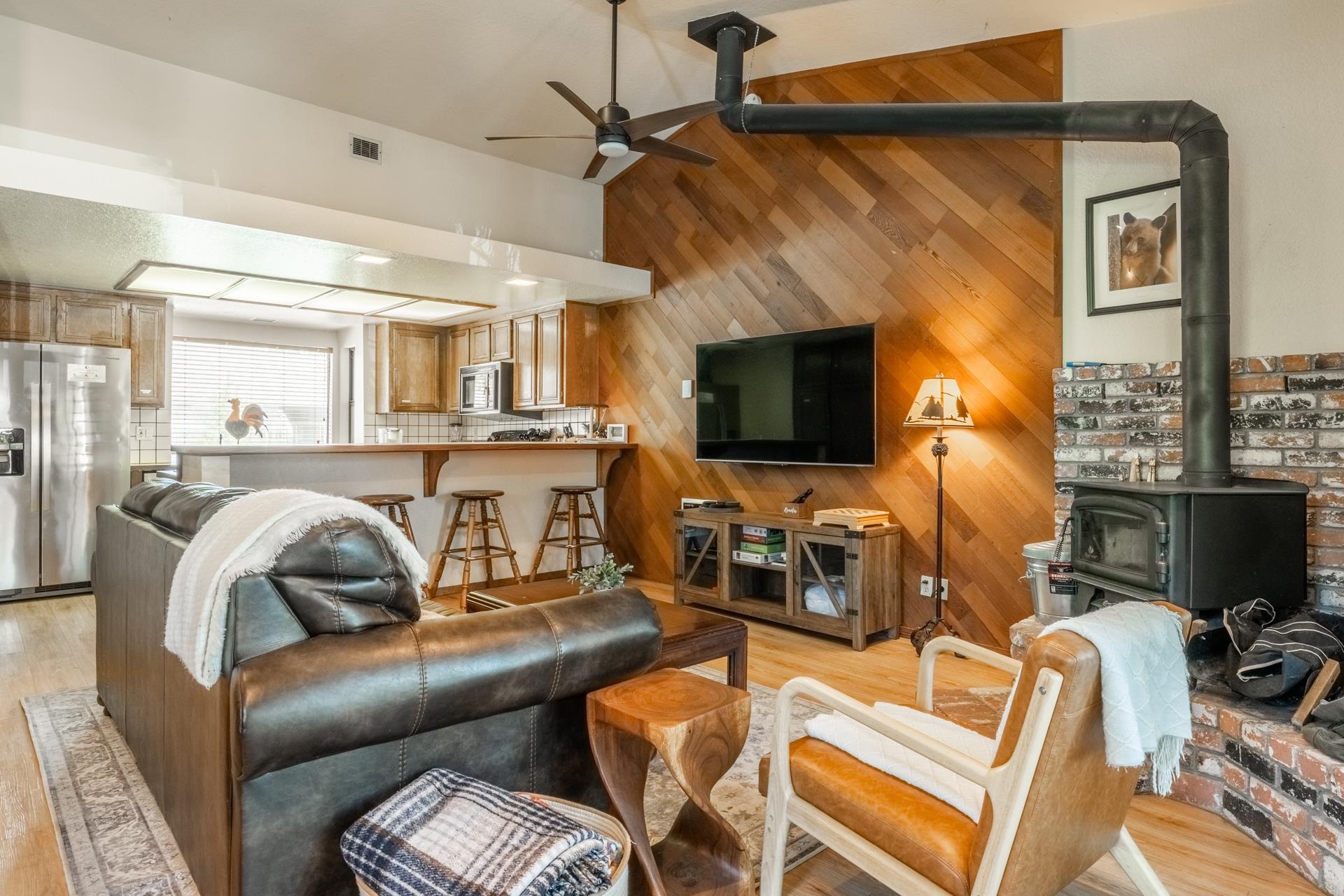 384 Joaquin Road, Unit 36 Mammoth Lakes, CA 93546 - Photo 6 of 36 Vaulted ceiling with a ceiling fan, wood-plank accent wall, brick-clad wood-burning stove with a metal chimney, L-shaped breakfast bar, and wood-finish flooring
