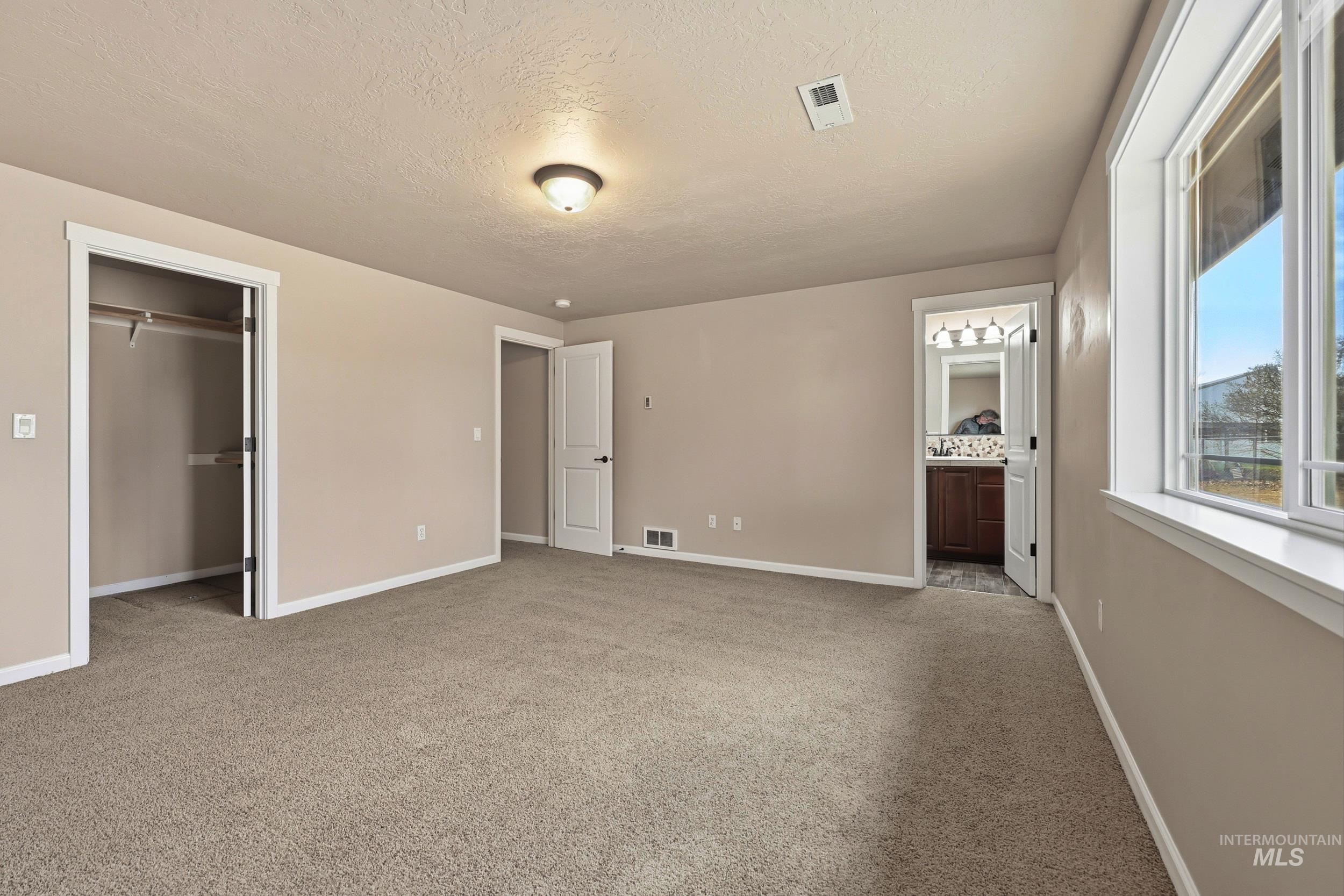 20203 Top Road Greenleaf, ID 83626 - Photo 11 of 16 Unfurnished bedroom featuring a textured ceiling, light carpet, a spacious closet, and ensuite bathroom