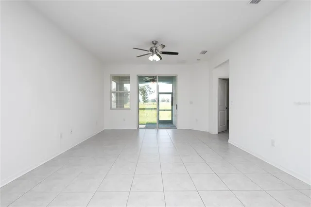 an empty room with chandelier fan and windows
