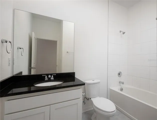 a bathroom with a granite countertop bathtub sink vanity mirror and toilet