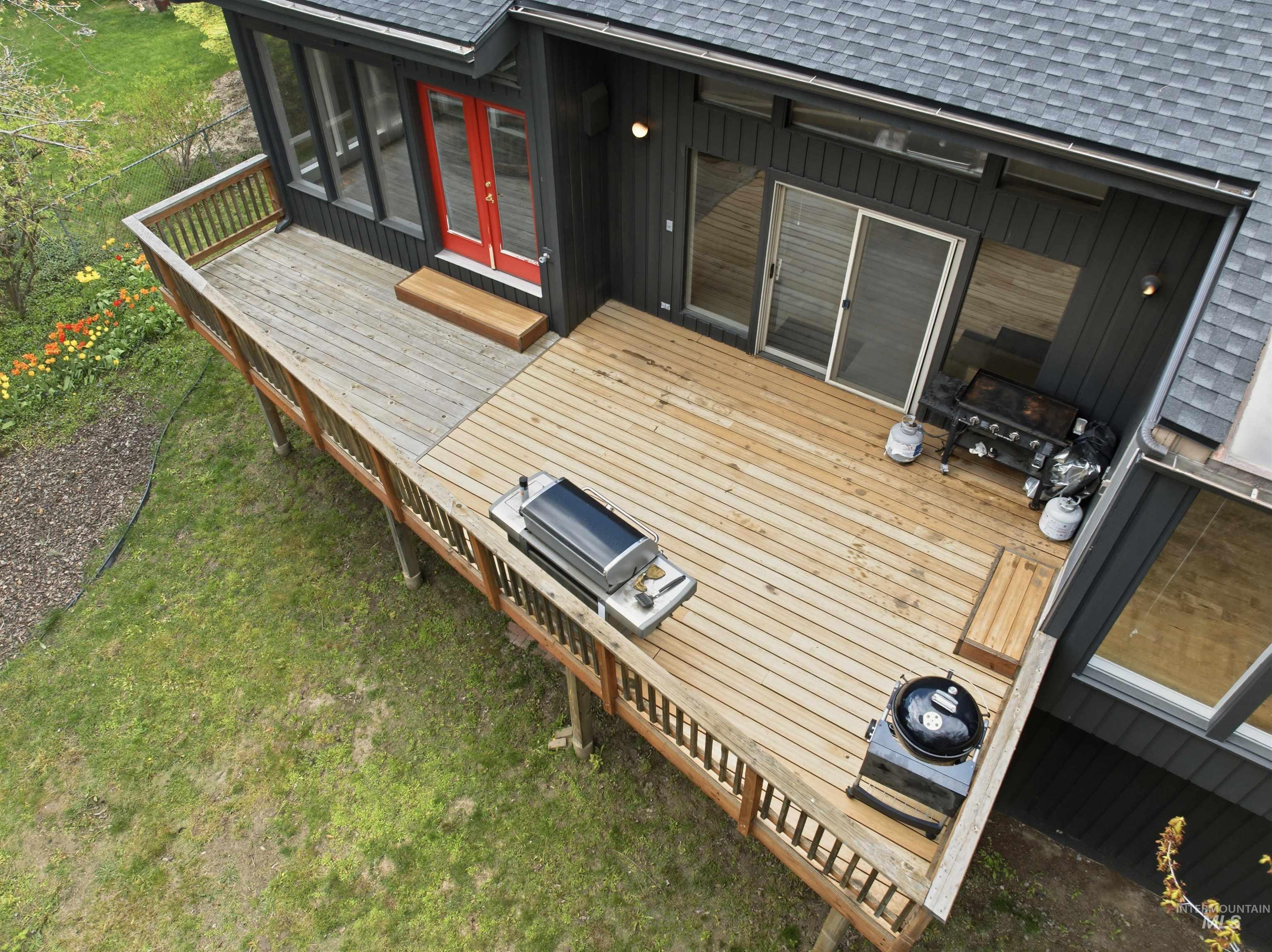 1540 Pine Cone Road Moscow, ID 83843 - Photo 43 of 49 Expansive wooden deck with railing, featuring a red entry door, a sliding glass door, and dark exterior siding