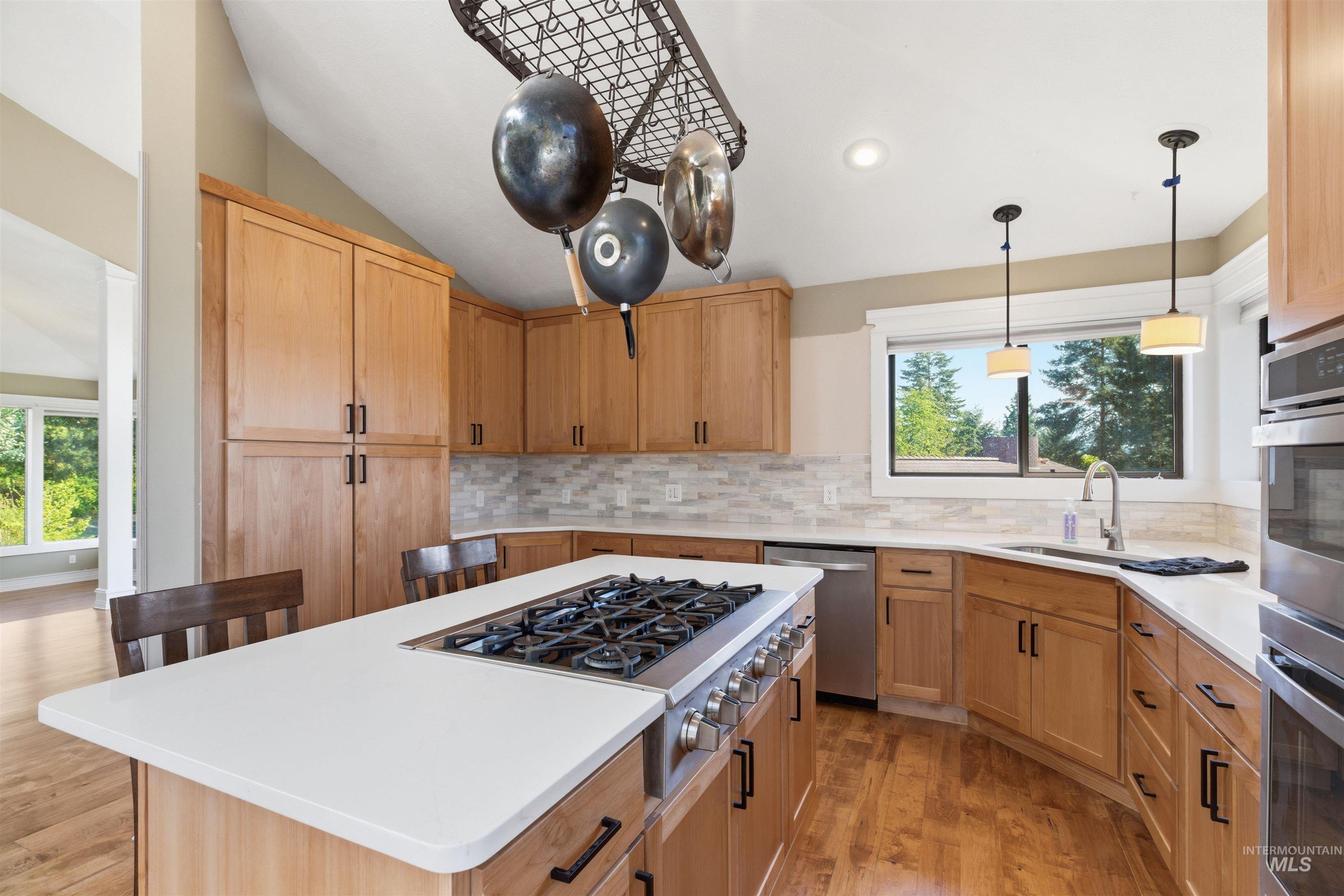 1540 Pine Cone Road Moscow, ID 83843 - Photo 9 of 49 Kitchen featuring a central island with a built-in range, light wood-finish cabinetry, white countertops, stainless steel appliances, and wood-finish flooring