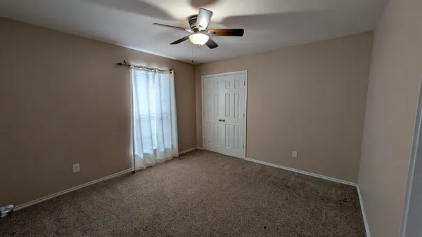 an empty room with chandelier fan and windows
