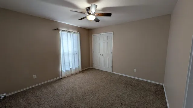 an empty room with chandelier fan and windows