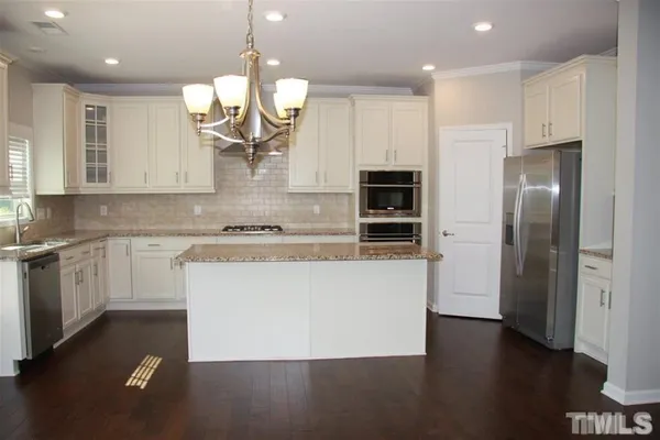 a large kitchen with granite countertop a white refrigerator a oven a sink and a island