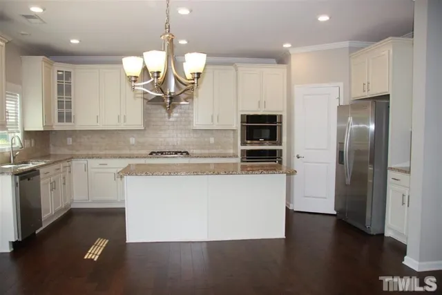 a large kitchen with granite countertop a white refrigerator a oven a sink and a island