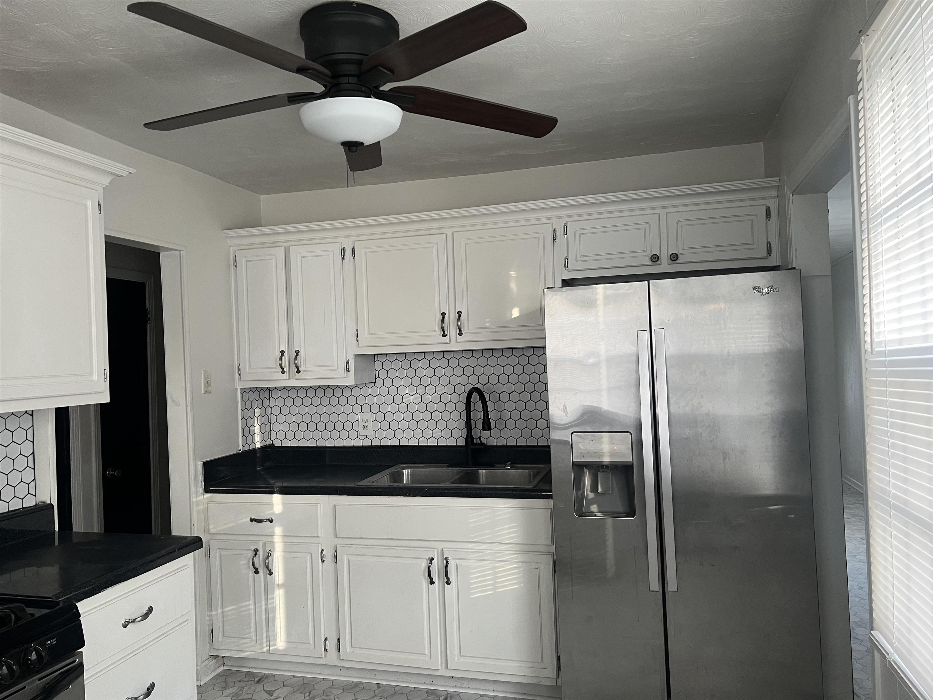 Kitchen with white cabinets, stainless steel fridge, decorative backsplash, and sink