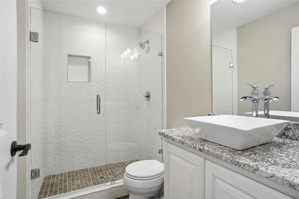 a bathroom with a granite countertop sink a toilet a mirror and shower