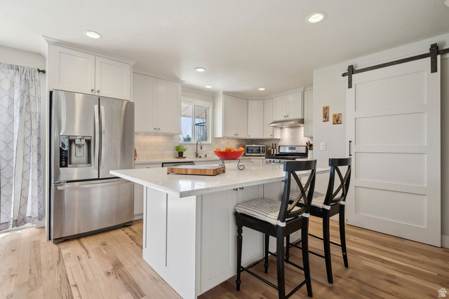550 Pine Canyon Road Midway, UT 84049 - Photo 11 of 44 Kitchen featuring white cabinetry, a center island with countertop seating, stainless steel appliances, wood-finish flooring, and a white barn door