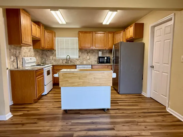 a kitchen with stainless steel appliances granite countertop a refrigerator a stove top oven a sink and dishwasher with wooden floor