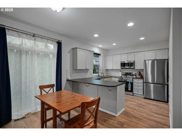 a kitchen with stainless steel appliances kitchen island granite countertop a refrigerator a sink a stove a dining table and chairs