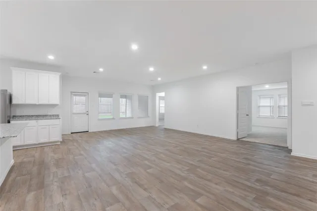 a view of empty room with wooden floor and kitchen