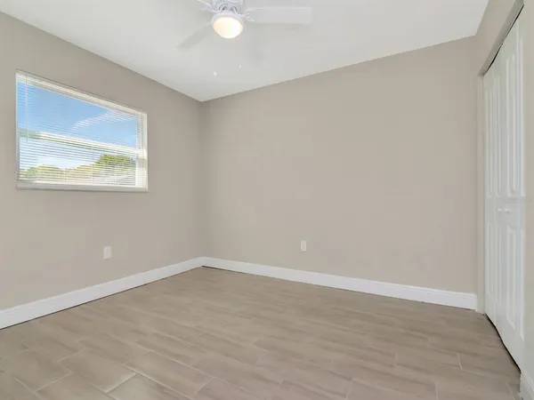 an empty room with wooden floor ceiling fan and window