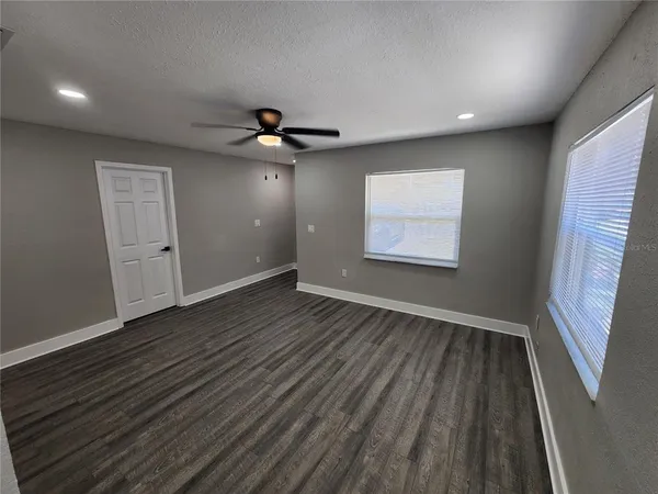 a view of an empty room with wooden floor and a ceiling fan