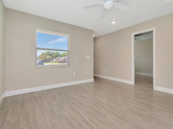 an empty room with wooden floor a ceiling fan and kitchen space