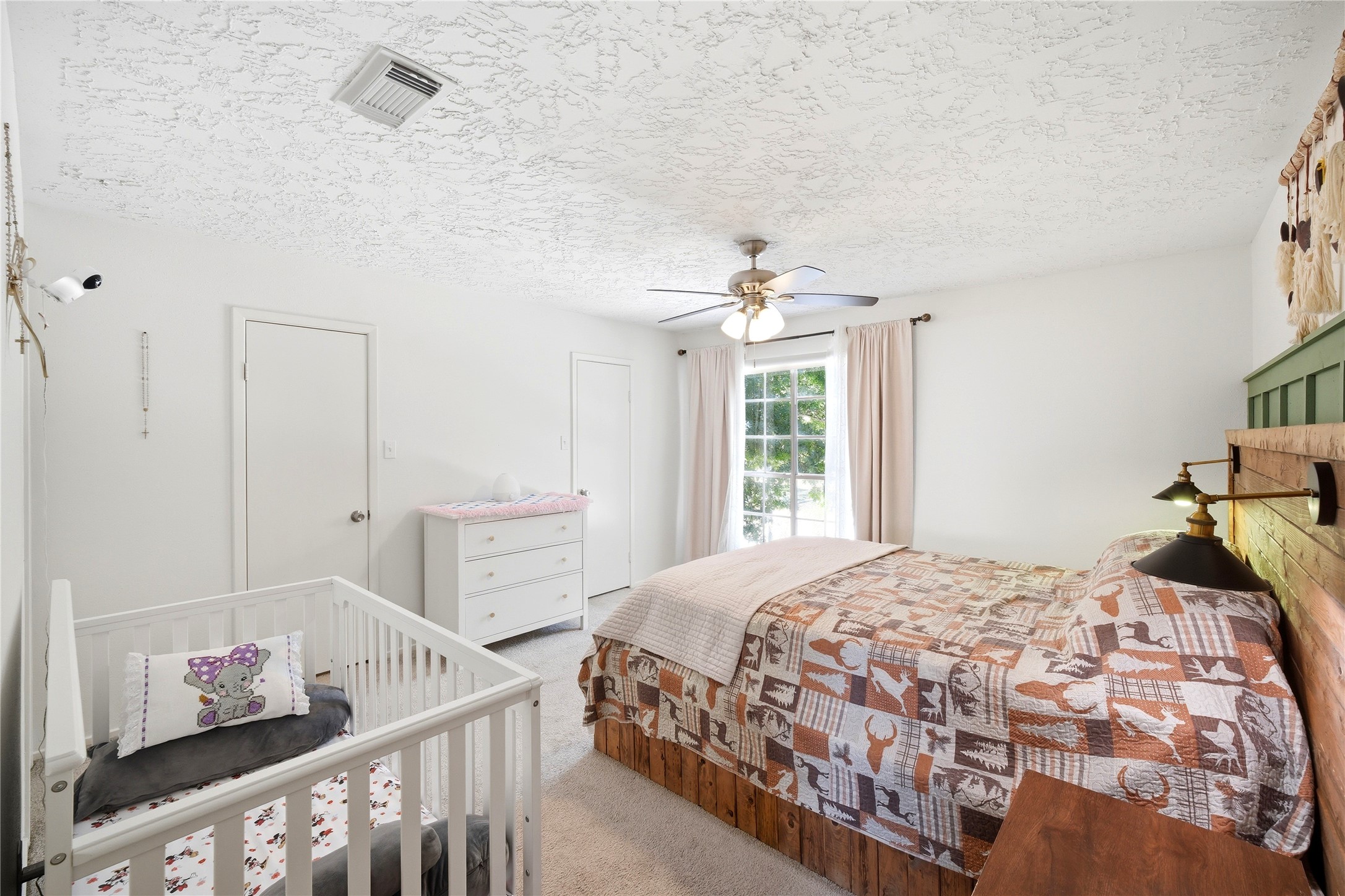 4718 Temple Bell Drive Spring, TX 77388 - Photo 33 of 50 This is a cozy bedroom featuring a large window with curtains, letting in natural light. It includes a comfortable bed with a patterned quilt, a ceiling fan, and a crib, making it ideal for a family. The room has a soft carpeted floor and a dresser for storage.