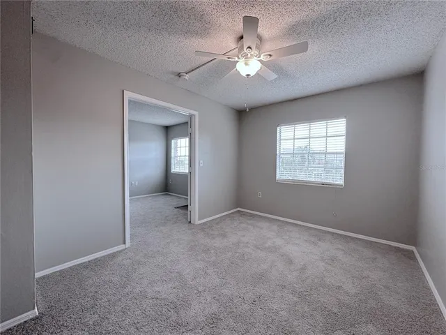 an empty room with chandelier fan and windows