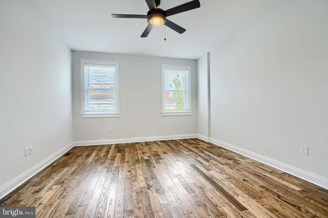 a view of empty room with wooden floor and fan