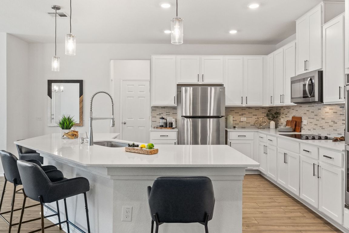 7808 Lawford Way Austin, TX 78744 - Photo 13 of 40 Kitchen with pendant lighting, appliances with stainless steel finishes, tasteful backsplash, white cabinets, and light wood-type flooring