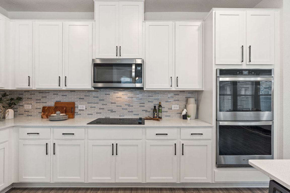 7808 Lawford Way Austin, TX 78744 - Photo 16 of 40 Kitchen with appliances with stainless steel finishes, white cabinets, tasteful backsplash, light stone countertops, and light wood-style flooring