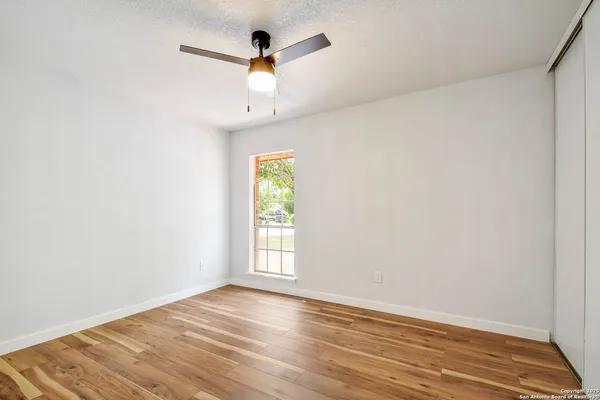 an empty room with wooden floor fan and windows
