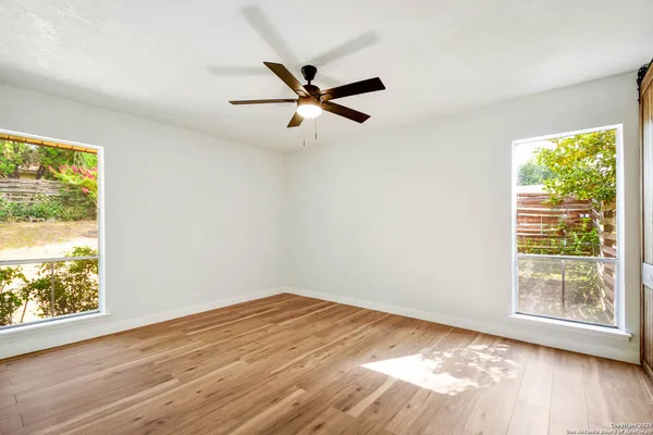 a view of a big room with wooden floor a ceiling fan and windows
