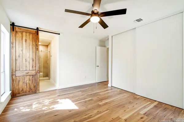 an empty room with wooden floor fan and windows