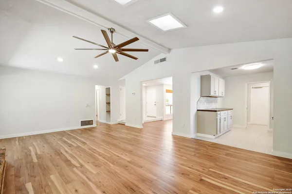 a view of empty room with wooden floor and kitchen view