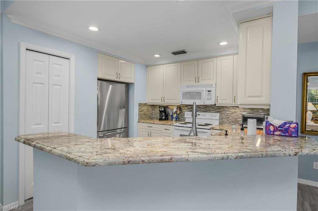 963 Egrets Run, Unit 102 Naples, FL 34108 - Photo 7 of 39 a kitchen with granite countertop kitchen island stainless steel appliances a sink refrigerator and cabinets