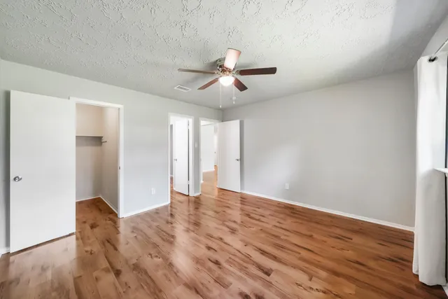 a view of an empty room with wooden floor and a ceiling fan