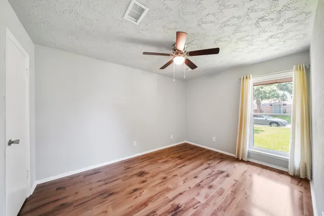 an empty room with wooden floor fan and windows