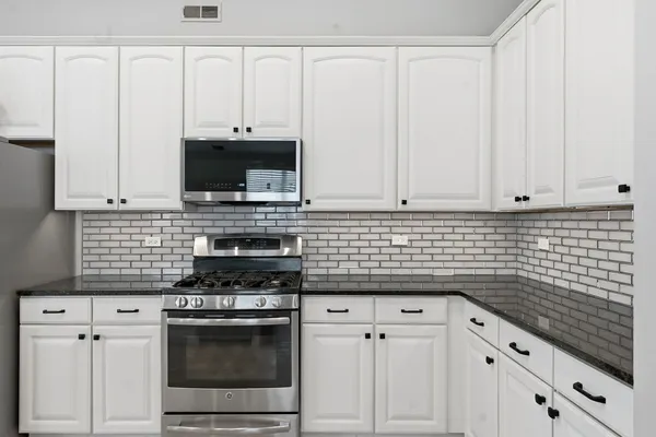 a large kitchen with granite countertop a stove a sink dishwasher and white cabinets with wooden floor