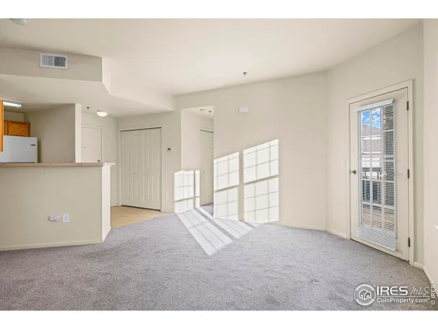 a view of an empty room with wooden floor and a kitchen