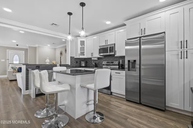 a kitchen with stainless steel appliances kitchen island granite countertop a refrigerator a stove and white cabinets with wooden floor