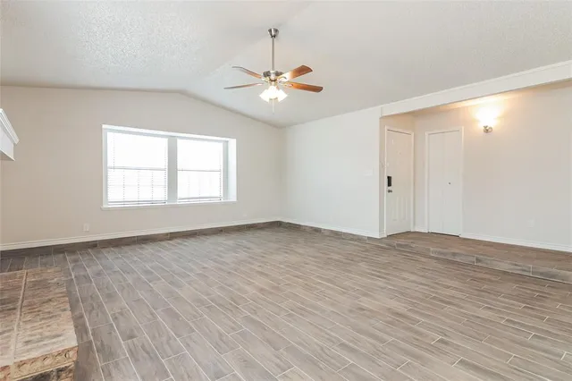 an empty room with wooden floor chandelier fan and windows