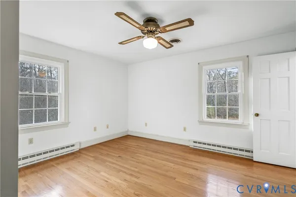 an empty room with wooden floor fan and windows