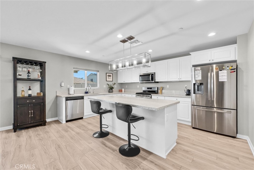 26538 San Jacinto Road Menifee, CA 92585 - Photo 11 of 34 a kitchen with stainless steel appliances kitchen island a refrigerator a stove a sink dishwasher and white cabinets with wooden floor