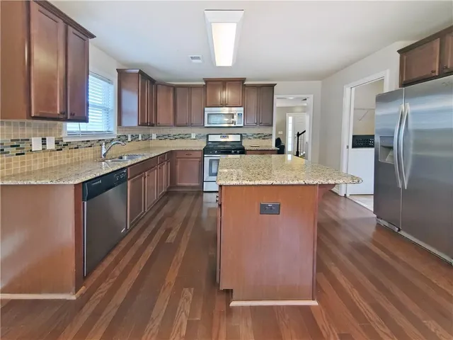 a large kitchen with stainless steel appliances granite countertop a refrigerator a sink dishwasher a s stove top oven a large island with wooden floor and cabinets