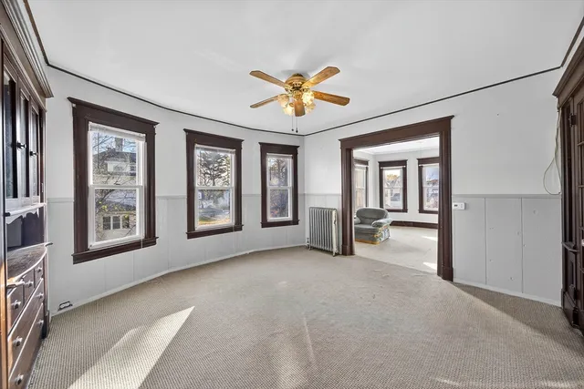 an empty room with chandelier fan and windows